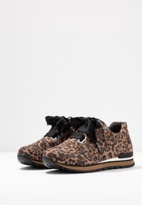 Des baskets à imprimé léopard présentent une texture semblable au daim, des lacets en ruban noir, une fermeture éclair latérale et une semelle extérieure noire avec un accent marron.