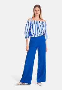 Off-the-shoulder top with blue and white stripes, paired with high-waisted blue wide-leg trousers and white striped slip-on shoes.