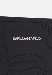 Surface en cuir noir avec un motif de logo perforé et une plaque de marque en métal argenté « KARL LAGERFELD » centrée près de la couture.