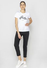 Biała koszulka z czarnym wzorem graficznym, zestawiona z dopasowanymi czarnymi spodniami i białymi trampkami. Prosty, casualowy strój odpowiedni na codzienne wyjścia.