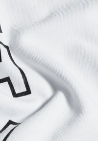 Witte stof met een gladde textuur, met zwart gedrukt tekst in vette lettertype, gedeeltelijk zichtbaar op een gekreukeld oppervlak.