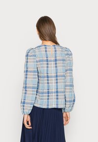 Niebieska i biała bluzka w kratę z bufkami, detalem w kształcie dziurki z tyłu i lekkim materiałem. Noszona z plisowaną granatową spódnicą.