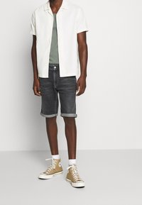 Valkoinen lyhythihainen nappikuorinen paita vihreän t-paidan päällä, yhdistettynä tummiin farkkushortseihin ja vaaleanbeigeihin korkeisiin tennareihin. Rentoa asustusta.