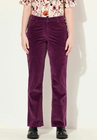 Pantalons en velours côtelé violets à coupe droite, avec un bouton à l'avant et des détails de poches. Portés avec un haut à motifs floraux.