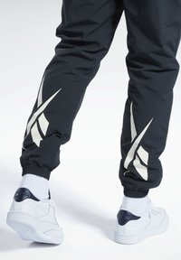 Marineblaue Sporthosen mit elastischen Bündchen haben weiße schräge Streifen. Kombiniert mit weißen Sneakers mit marineblauen Akzenten und weißen Crew-Socken.