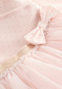 Měkké růžové dětské šaty s drobným tečkovaným vzorem, průhlednou nařasenou sukní, zlatou bordurou a detailním látkovým mašlí.