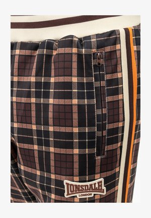 Brązowe i czarne dżinsowe joggery z elastycznym pasem, boczną kieszenią na zamek i naszywką z logo. Charakteryzują się kontrastującymi bocznymi paskami w kolorze cynamonowym i pomarańczowym.