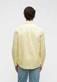 Lys gul langærmet skjorte med ryg yoke, knapmanchetter og en buet kant, parret med lyseblå denim jeans.