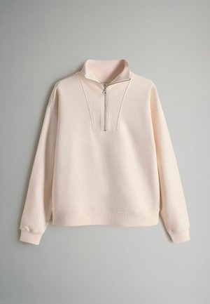 Light pink sweatshirt with a high collar, half-zip closure, and ribbed accents. Features long sleeves and a relaxed fit. Soft texture.
