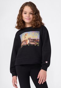 Zwarte sweatshirt met een geprinte "GOLDEN Hour" graphic in geel en blauw. Bevat een logo op de mouw en heeft een relaxte pasvorm. Gecombineerd met zwarte leggings.