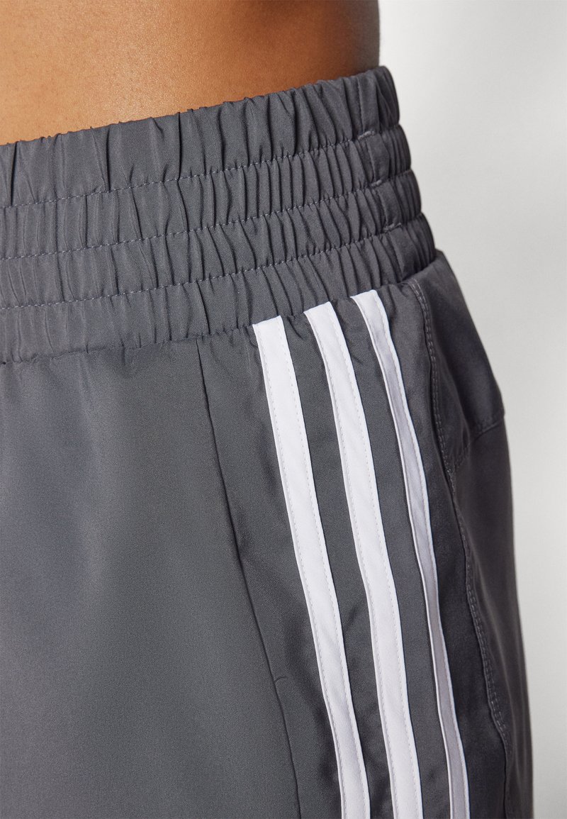 Graue Sportshorts mit einem elastischen Bund, strukturiertem Stoff und drei weißen Streifen an der Seite als Akzent.
