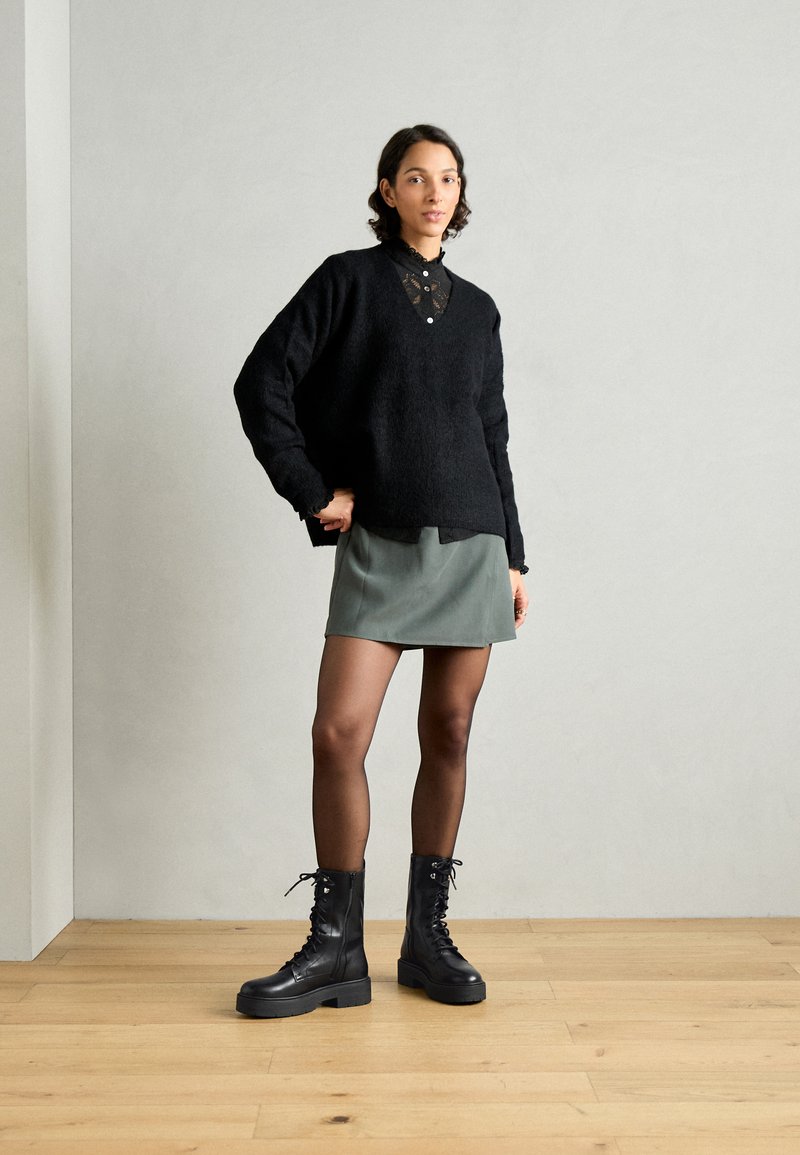 Czarny sweter o teksturowanej powierzchni z kołnierzykiem zdobionym koronką, nałożony na zieloną mini spódniczkę. Uzupełniony czarnymi, lace-up wojskowymi butami.