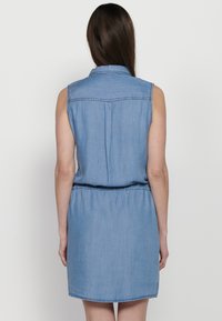 Abito in denim di un blu chiaro, senza maniche, con colletto, vita cin cinata e orlo stondato. Sul retro presenta un yoke e dettagli a pieghe.