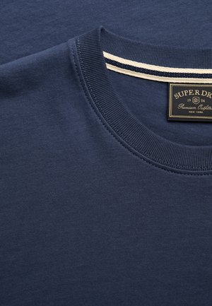 Fløjlblå crew neck t-shirt med ribbet krave og et sort mærkat med teksten "Superdry Premium Outfitter New York" indeni kraven.