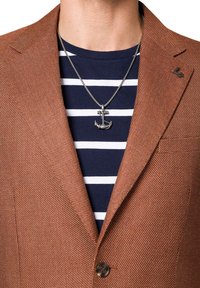 Brązowy blazer o teksturowanej powierzchni z klapami, noszony na niebieskiej koszuli w paski. Posiada srebrny wisiorek w kształcie kotwicy oraz małą emblemat na klapie.