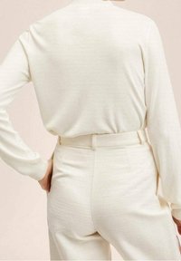 Maglietta a maniche lunghe color crema con un taglio rilassato e una texture liscia abbinata a pantaloni alto in vita dello stesso colore.