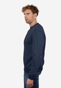 Sudadera azul marino con cuello redondo y tejido texturizado. Presenta un detalle en el pecho delantero con puños y bajo acanalados.