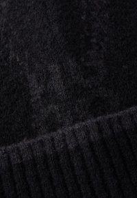 Tissu tricoté noir avec une finition douce et texturée. Présente des détails côtelés sur le bord, créant un effet superposé et un motif subtil.