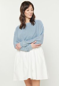 Tricou cu dungi albastre și albe, cu mânecă lungă, asortat cu o fustă albă pliată. Tricoul are o croială lejeră și o textură ribbată.