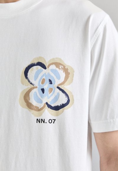 Hvid bomulds T-shirt med et farverigt blomsterdesign i blå, brun og creme. Har teksten "NN. 07" under grafik.