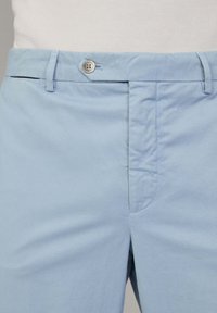 Chinos in cotone azzurro chiaro con una texture liscia, dotati di chiusura con bottone in metallo e passanti per la cintura, e un design a davanti piatto.