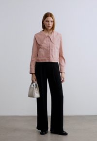 Μια κοντή ροζ τζιν μπουφάν με μεγάλο γιακά και μπροστινές τσέπες, συνδυασμένη με μαύρο παντελόνι φαρδιάς γραμμής και μια μικρή λευκή τσάντα.