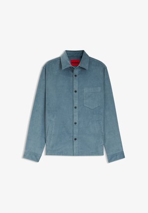 Camicia in velluto a coste azzurro chiaro con chiusura frontale a bottoni, colletto a punta, taschino sul petto e due tasche laterali. Bottoni neri e texture a coste.