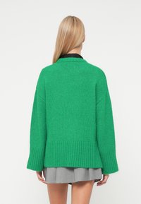 Πράσινο πλεκτό πουλόβερ με χαλαρή εφαρμογή, φαρδιές μανίκες και ριμπ τελείωμα. Η υφή είναι απαλή, με μεσαία παThickness για ζεστασιά.