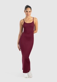 Vestido maxi burdeos con textura acanalada, tirantes finos y silueta ajustada; aberturas laterales en el dobladillo; combinado con zapatillas blancas.