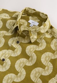 Chemise boutonnée vert olive avec motif géométrique circulaire blanc et col plié, taille moyenne, étiquette de marque "NEXT" visible.
