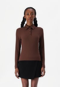 Brown ribbed long-sleeve polo shirt with a collar and three dark buttons, paired with a black wrap skirt. Smooth texture, fitted design.