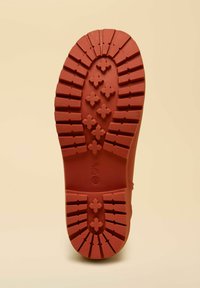 Suola di scarpa rossa in gomma con scanalature profonde e motivi a croce. Bordi lisci e tacco circolare. Sfondo semplice.