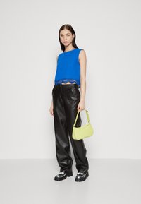 Blå kort crop-top med blonderkant, kombinert med svarte, syntetiske skinnbukser og en liten limegrønn håndveske. Svarte platåsko med sølvfargede detaljer.