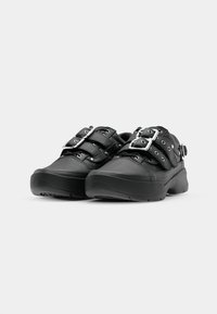 Black sneakers with a textured leather upper, featuring two wide straps, silver-tone buckles, and a thick rubber sole with tread pattern.