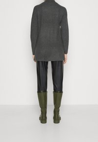 Grijze gebreide lange trui, zwarte leren-achtig pantalons en groene kniehogere laarzen met ritsen aan de achterkant. Eenvoudig, functioneel ontwerp.