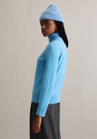 Lichtblauwe coltrui van zacht materiaal met lange mouwen en geribbelde zoom, gecombineerd met een bijpassende gebreide muts.