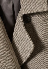 Bruin gestreepte jasstof met een gestructureerde afwerking. Voorzien van een reverskraag en een glanzende zwarte knoop, met een binnenvoering in een donkere tint.