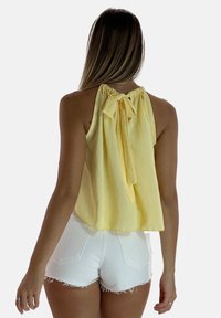Top giallo a halter con una vestibilità morbida, scollatura arricciata e dettaglio a fiocco sul retro, abbinato a pantaloni corti bianchi a vita alta.