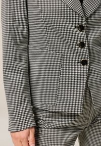 Zwart-wit houndstooth patroon blazer met een geknipt kraag, vier knopen en twee zijzakken. Soepele textuur en getailleerde pasvorm.