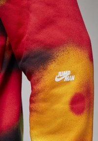 Manche tie-dye rouge et jaune avec texte blanc « Jump Man » et logo swoosh sur le tissu.