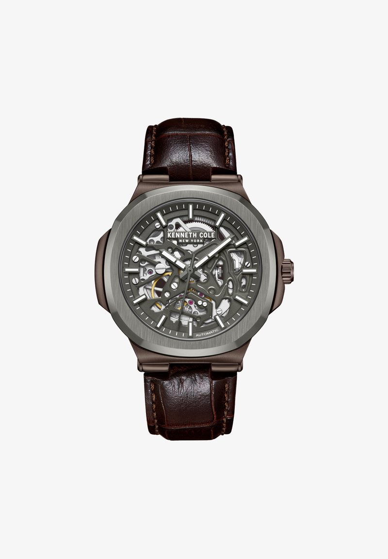 Orologio automatico skeleton con cassa rotonda grigia, quadrante trasparente che rivela il movimento, cinturino in pelle marrone e dettagli argentati.