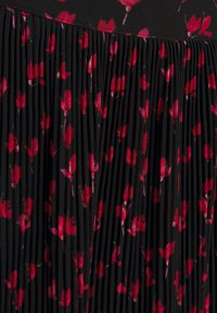 Falda plisada de tela negra adornada con un patrón floral rojo. Presenta plisados finamente estructurados para textura y movimiento.