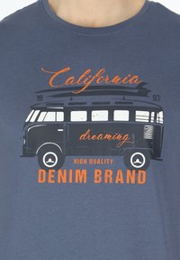 Navy blue t-shirt featuring a graphic of a vintage van. Text includes "California dreaming" and "Denim Brand" in orange and black.