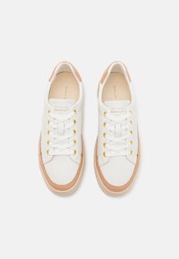 Paire de baskets GANT blanches et beiges avec des lacets blancs et des œillets dorés, vues de dessus sur un fond clair uni.