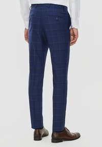 Granatowe spodnie w kratę o dopasowanym kroju, z dwoma tylnymi kieszeniami z guzikami i subtelną fakturą. Klasyczny fason z płaskim przodem.