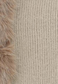 Maglione di maglia color beige chiaro con trama a costine verticali, caratterizzato da un morbido dettaglio in pelliccia marrone sul lato sinistro.