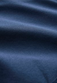 Tissu texturé bleu foncé avec des plis doux et des ombres créant une surface lisse et légèrement ondulée.