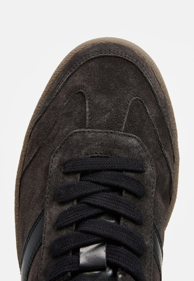 Baskets noires en daim avec orteil arrondi, empeigne texturée, lacets noirs, accents en cuir contrastés et semelle en caoutchouc.