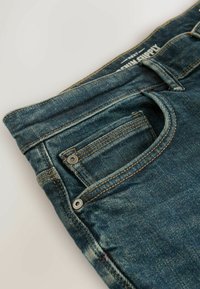 Blå denim jeans med et klassisk design, der har en lille forside lomme, metal knap detaljer og synlige sy detaljer.