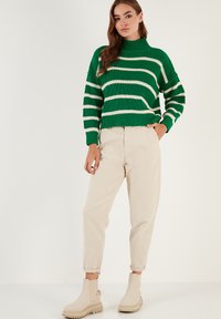Maglione a righe verdi in maglia con collo alto, abbinato a pantaloni beige a sigaretta e stivaletti beige alla caviglia. Tessuto strutturato, vestibilità rilassata.